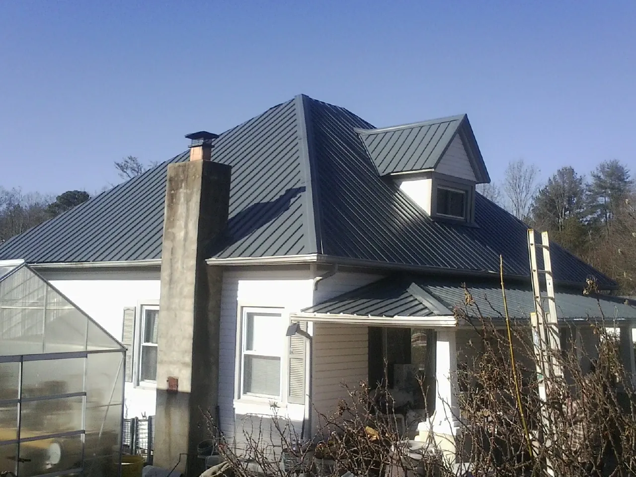 Dark blue standing seam metal roof on a white farmhouse with dormer — Slate & Tile Roof Repair by Roofing Brothers in Muldoon