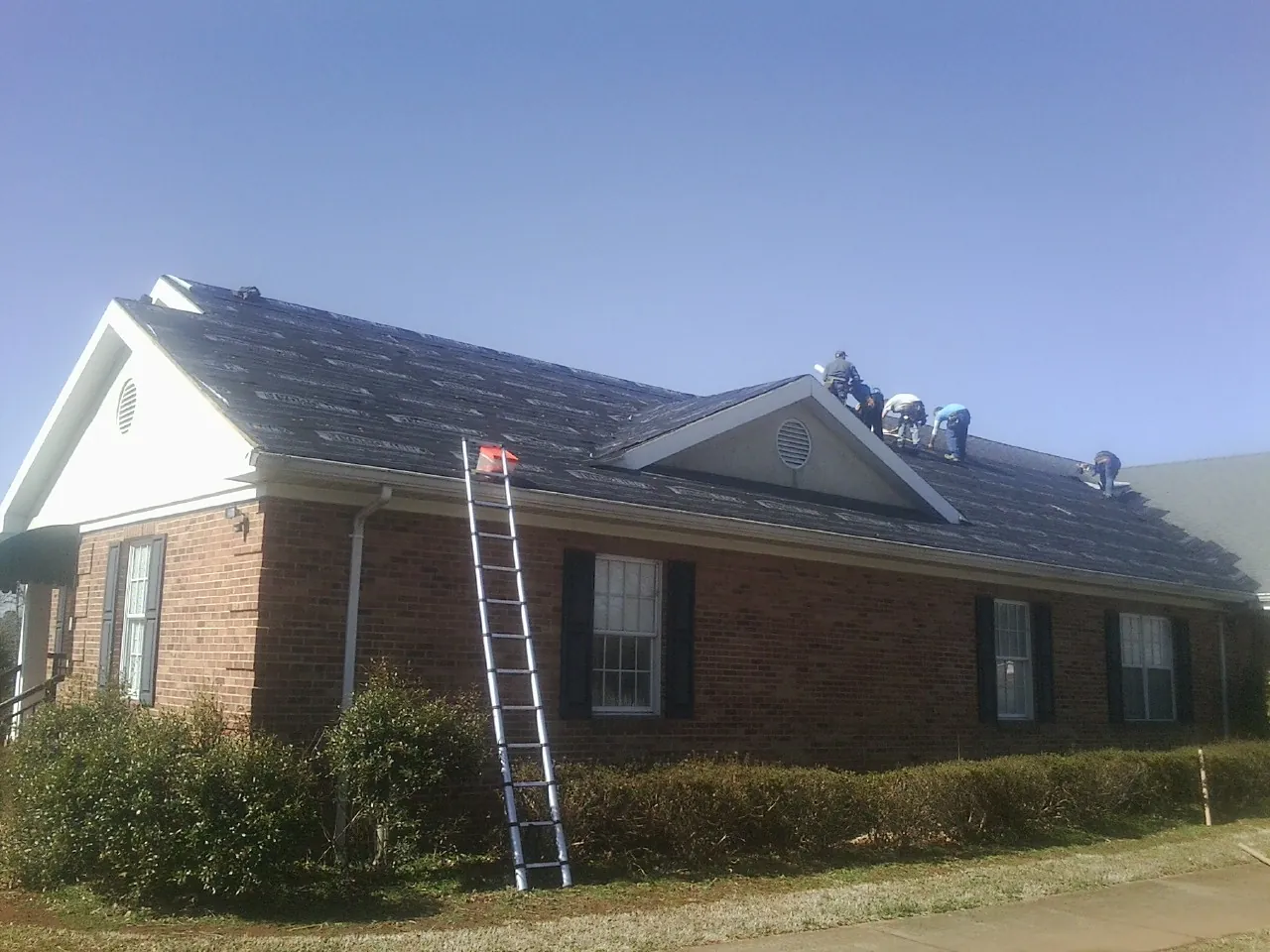 Crew tearing shingles off a brick ranch roof with a ladder set — Metal Roof Repair work by our crew in Muldoon