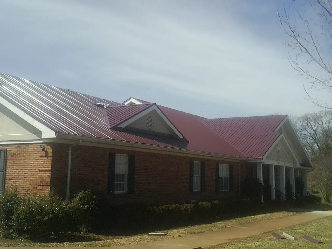Red metal roof with gabled entries on a long brick building, from a Hail Damage Roof Repair job in Muldoon