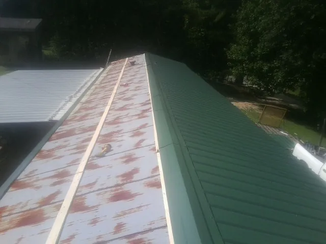 Old rusted panels beside newly installed green metal roofing — Wind Damage Roof Repair by Roofing Brothers in Muldoon
