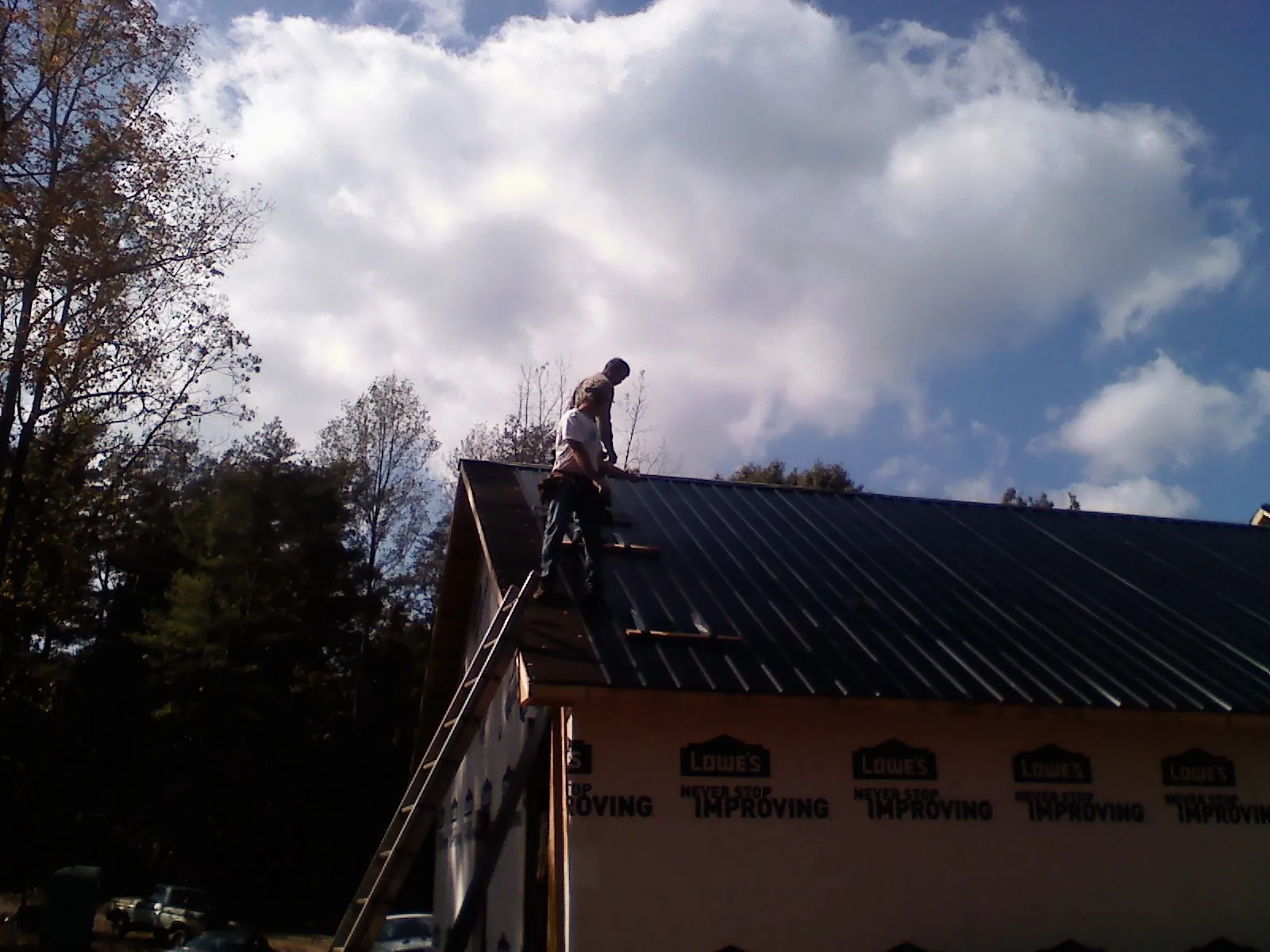 Roofer fastening dark metal panels high against a cloudy sky, from a Roof Inspection job in Muldoon