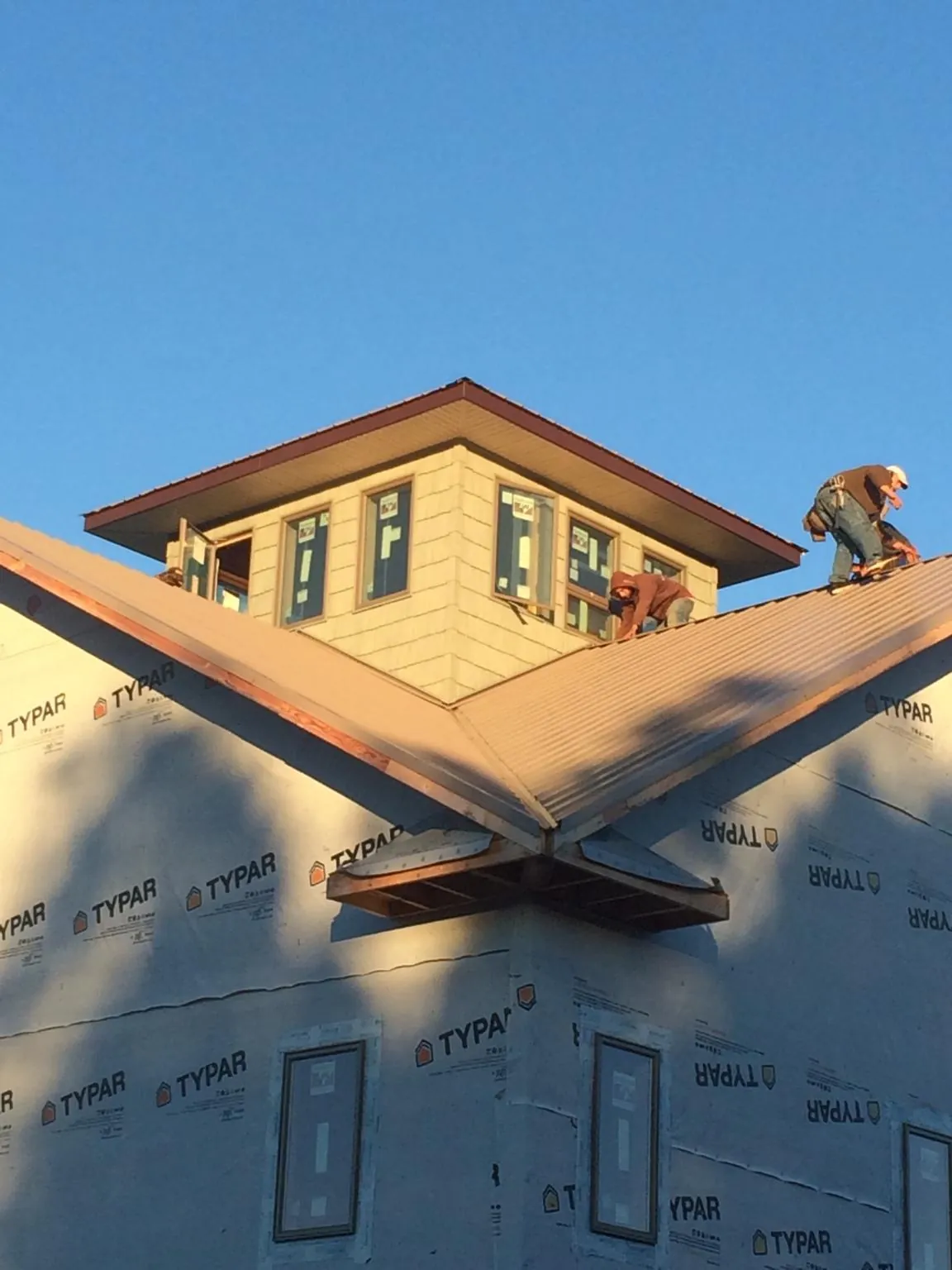 Roofers working around a rooftop cupola on a new metal roof at sunset — Roof Waterproofing in Muldoon by Roofing Brothers
